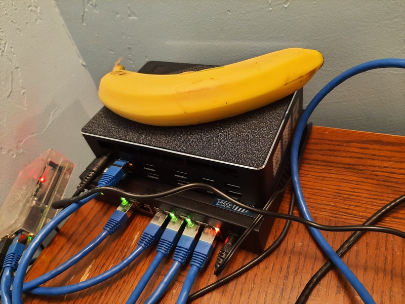 A stack of things: switch on the bottom, mini PC in the middle, and a banana on top, for scale. The banana is larger than the mini PC.